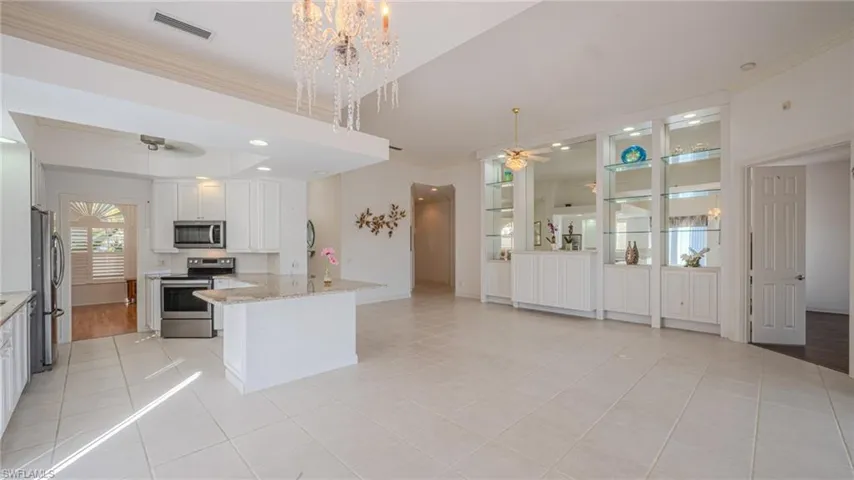 Kitchen featuring white cabinets, a ceiling fan, stainless steel appliances, crown molding, and light stone countertops