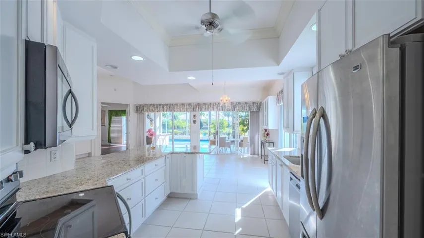 Kitchen with a peninsula, stainless steel appliances, crown molding, white cabinetry, and light stone countertops