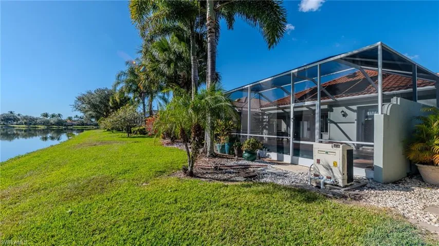 Back of property featuring a sunroom, a lanai, a yard, and a water view