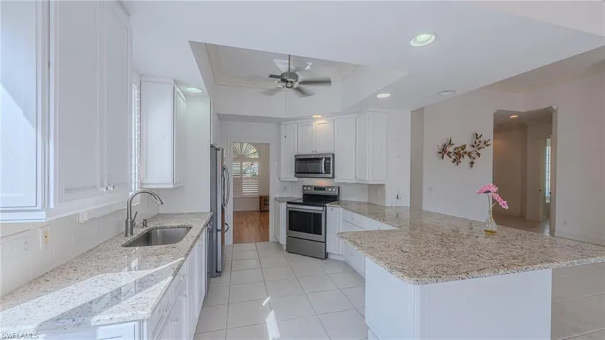 Kitchen featuring crown molding, white cabinetry, light stone countertops, appliances with stainless steel finishes, and a peninsula