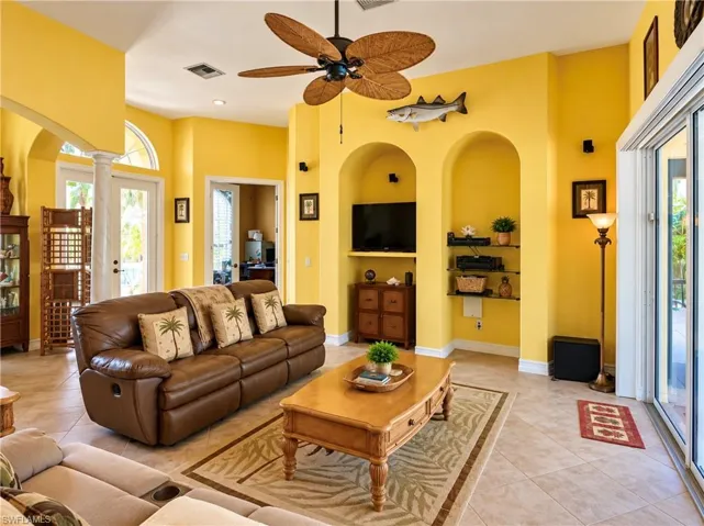 Living area featuring dual built-in arched alcoves, high ceilings, ceiling fan with palm-style blades, ceramic tile flooring, and multi-panel sliding glass doors
