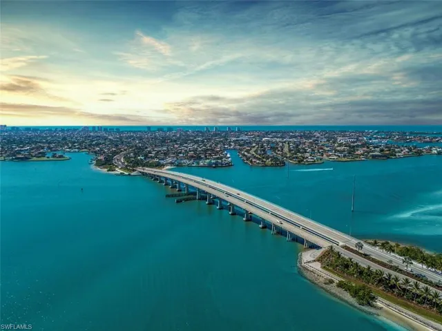 Aerial perspective of waterfront surroundings featuring coastal waterways, an expansive bridge, and proximity to the open ocean horizon