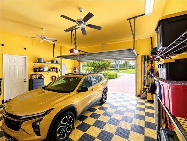 Garage featuring checkered modular flooring, dual ceiling fans, wall-mounted metal shelving units, and a pedestrian door