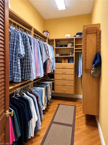 Walk-in closet featuring floor-to-ceiling wooden cabinetry, five integrated storage drawers, multiple hanging rods, and wood-finish flooring in a herringbone pattern