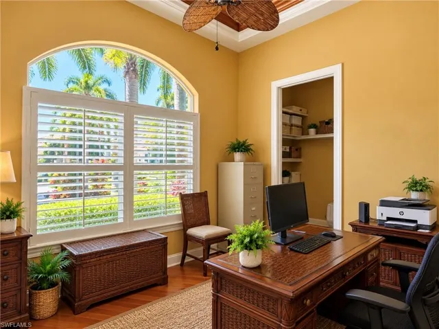 Arched window with plantation shutters, coffered ceiling with a wood-finish ceiling fan, and built-in shelving