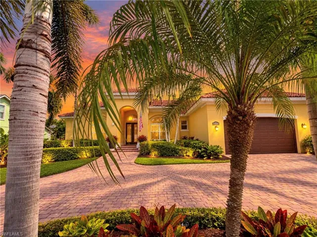 Single-story residence featuring a terracotta-tiled roof, stucco facade, arched entryway, paved driveway, and mature palm landscaping