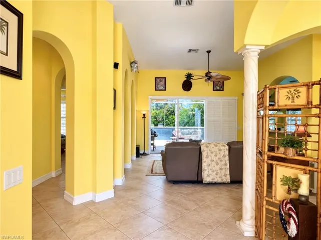 Ceramic tile flooring, decorative arched doorways, prominent column with spiral detailing, ceiling-mounted paddle fan, and large sliding glass doors