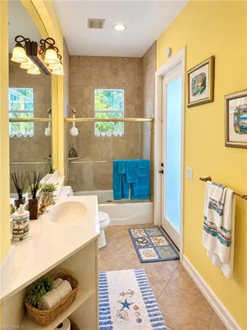 Bathroom featuring a tiled tub-shower combination with a sliding glass door, vanity with a white countertop, wall-to-wall mirror, and an exterior door with frosted glass