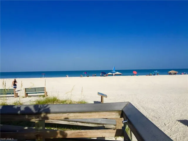 Wooden boardwalk with a handrail, integrated metal-capped railing, and direct sand access to a white-sand beach