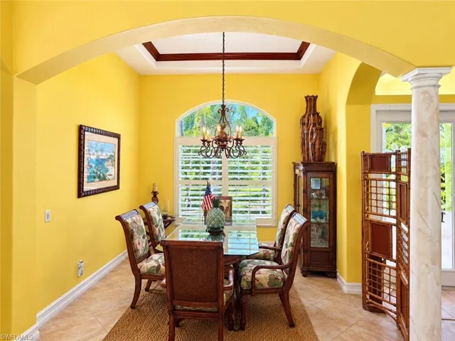 Arched entryway featuring a decorative column, coffered ceiling, ceramic tile flooring, and a central arched window with plantation shutters