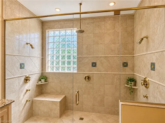 Walk-in shower featuring floor-to-ceiling tile, a frameless glass enclosure, a built-in stone bench, dual showerheads with an overhead rainfall fixture, and a decorative glass block window