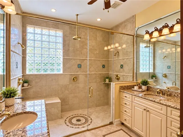 Bathroom featuring a walk-in shower with glass enclosure, built-in tile bench, rain showerhead, stone-finish countertops, and decorative tile accent inlay