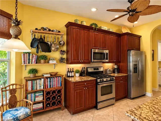 Kitchen featuring warm-toned wood cabinetry, stone countertops, stainless steel appliances, recessed lighting, and a decorative ceiling fan