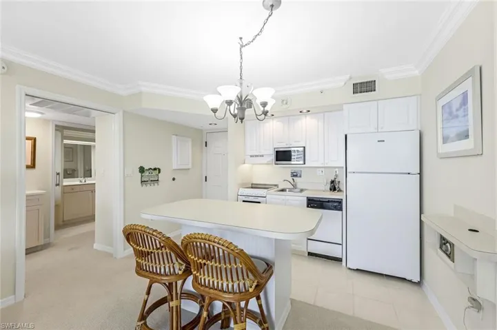 Kitchen with white appliances, a chandelier, a sink, a breakfast bar area, and light countertops