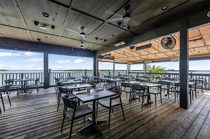 Wooden terrace with a water view, outdoor dining area, and ceiling fan