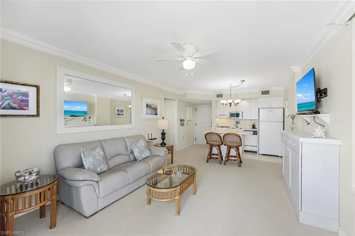 Living room featuring ceiling fan, ornamental molding, light carpet, a chandelier, and baseboards