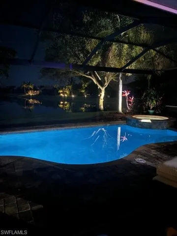 Pool at night featuring glass enclosure and an in ground hot tub