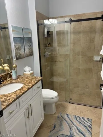 Bathroom featuring tile patterned flooring, a shower with shower door, vanity, and toilet