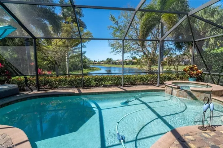 View of swimming pool with an in ground hot tub, glass enclosure, and a water view