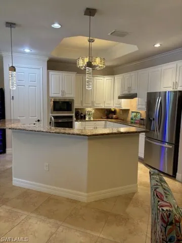Kitchen with an inviting chandelier, fridge, white cabinetry, and decorative light fixtures