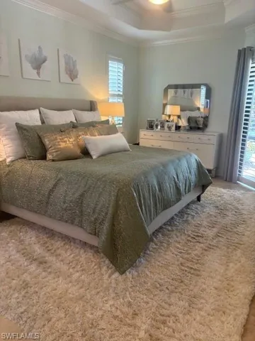Bedroom with ornamental molding, a tray ceiling, multiple windows, and ceiling fan