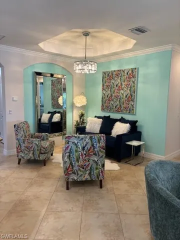Living room with a tray ceiling, a chandelier, and ornamental molding
