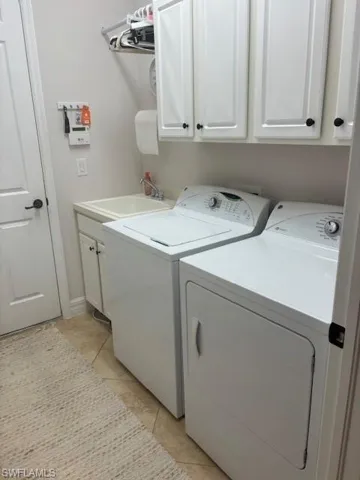 Laundry area with washing machine and dryer, sink, light tile patterned floors, and cabinets
