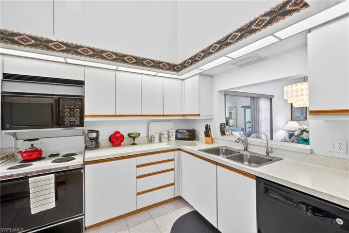 Dual tone kitchen with two tone cabinets, black appliances, light countertops, and light tile patterned floors