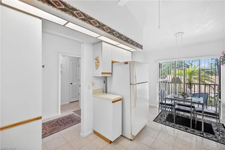Kitchen featuring freestanding refrigerator, light countertops, white cabinets, light tile patterned floors, and vaulted ceiling