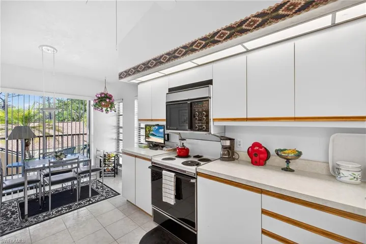 Kitchen with light countertops, black appliances, two tone cabinetry, light tile patterned floors, and hanging light fixtures