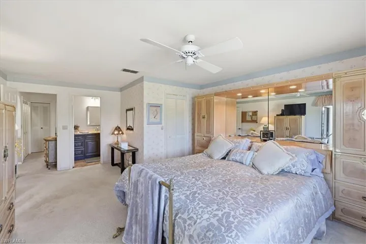 Bedroom with wallpapered walls, light colored carpet, ceiling fan, and ensuite bath
