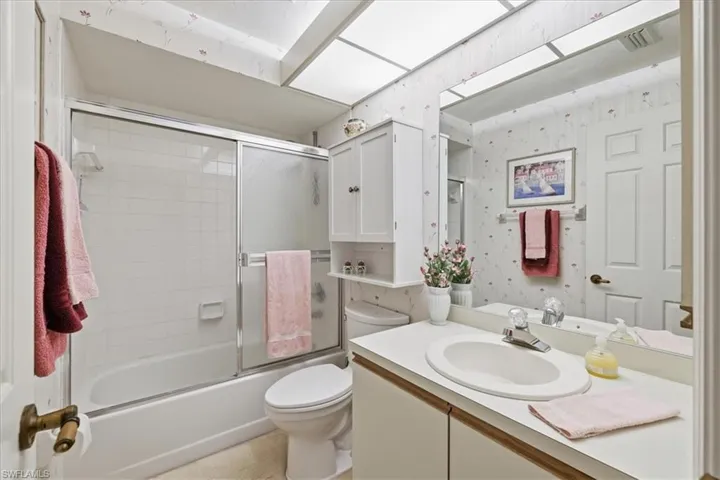 Full bathroom with wallpapered walls, vanity, and enclosed tub / shower combo