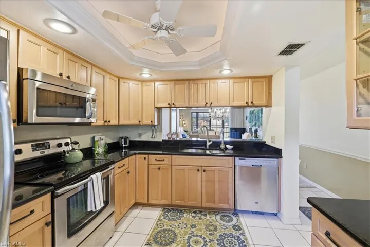 Kitchen featuring stainless steel appliances, ornamental molding, a ceiling fan, light tile patterned flooring, and dark stone counters