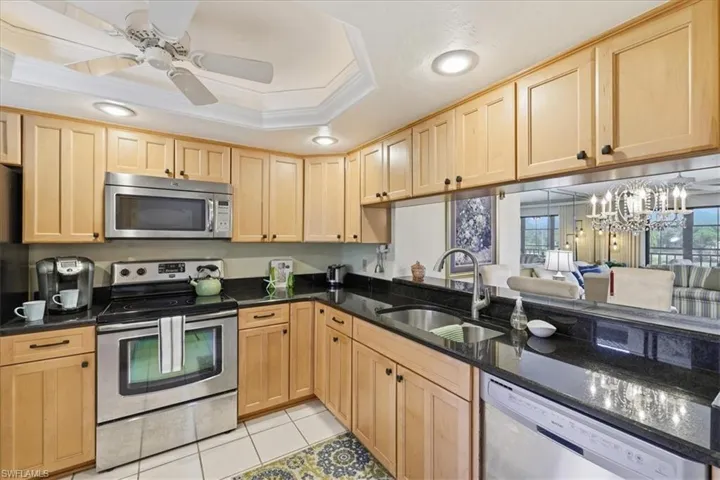 Kitchen featuring ceiling fan, stainless steel appliances, crown molding, dark stone counters, and a chandelier