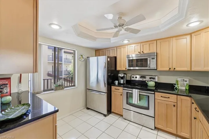 Kitchen with stainless steel appliances, crown molding, a ceiling fan, dark stone counters, and light wood finish cabinetry