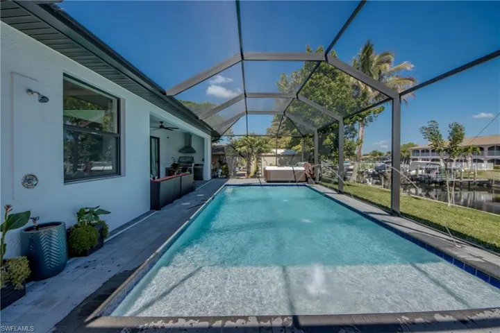 Swimming pool featuring a patio area, a sunroom, glass enclosure, a water view, and a lawn