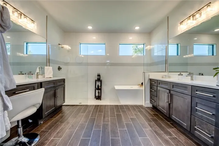 Full bathroom with tile walls, two vanities, a soaking tub, healthy amount of natural light, and wood tiled floors