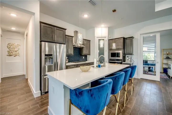 Kitchen with a kitchen island with sink, stainless steel appliances, a kitchen bar, wood finish floors, and pendant lighting