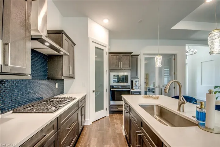 Kitchen featuring dark wood finish cabinetry, stainless steel appliances, wood tiled floors, light stone countertops, and tasteful backsplash