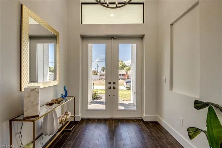 Doorway with wood finished floors, healthy amount of natural light, french doors, a chandelier, and a textured wall