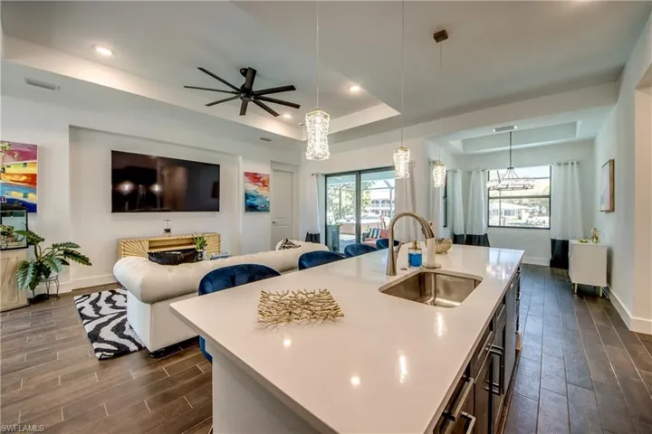 Kitchen featuring a raised ceiling, wood tiled floors, a kitchen island with sink, ceiling fan, and hanging light fixtures