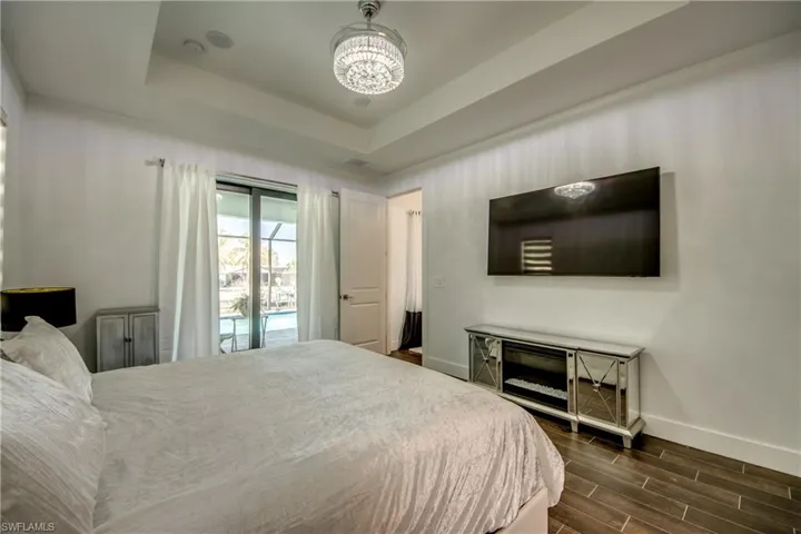 Bedroom with wood finish floors, access to exterior, hanging lights, and a raised ceiling