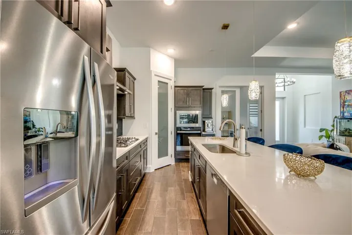 Kitchen with stainless steel appliances, dark wood finish cabinets, wood finish floors, and light stone countertops