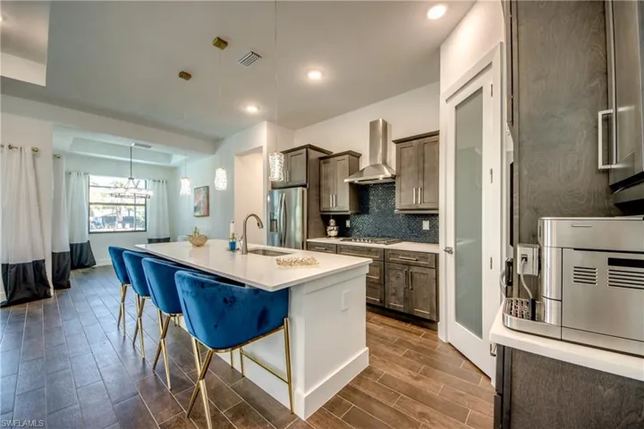 Two tone kitchen featuring a kitchen bar, a center island with sink, wood finish floors, decorative backsplash, and stainless steel appliances