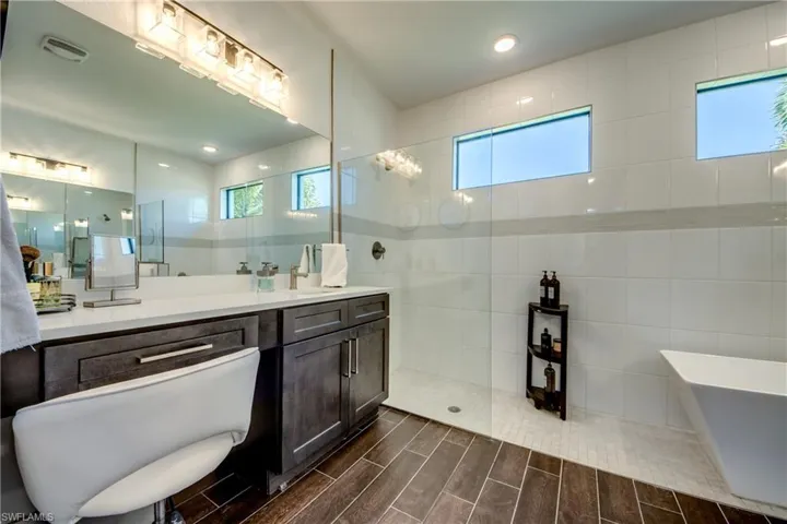 Full bath featuring wood tiled floors, a freestanding tub, walk in shower, tile walls, and vanity