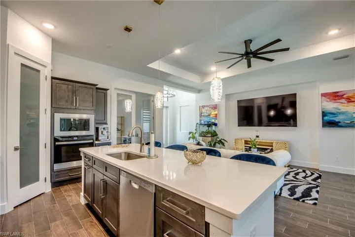 Kitchen with dark wood finish cabinetry, wood finish floors, stainless steel appliances, open floor plan, and an island with sink
