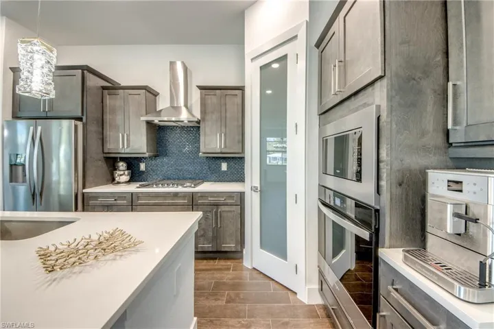 Kitchen with stainless steel appliances, decorative backsplash, light stone counters, wood finish floors, and pendant lighting