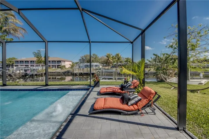 Swimming pool featuring a water view, a sunroom, a lawn, and glass enclosure