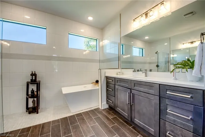 Full bath featuring vanity, tile walls, a soaking tub, walk in shower, and wood finish floors