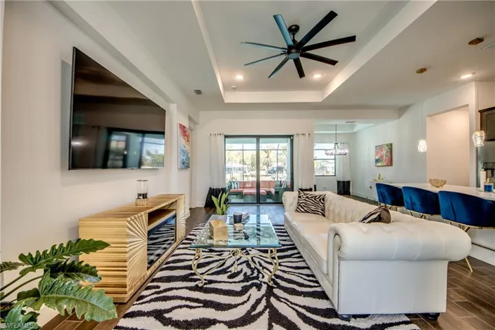 Living area featuring ceiling fan, wood finish floors, a raised ceiling, and recessed lighting